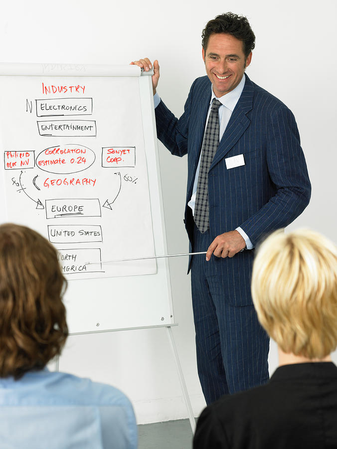 Businessman giving presentation, smiling, colleagues in foreground Photograph by John Rowley