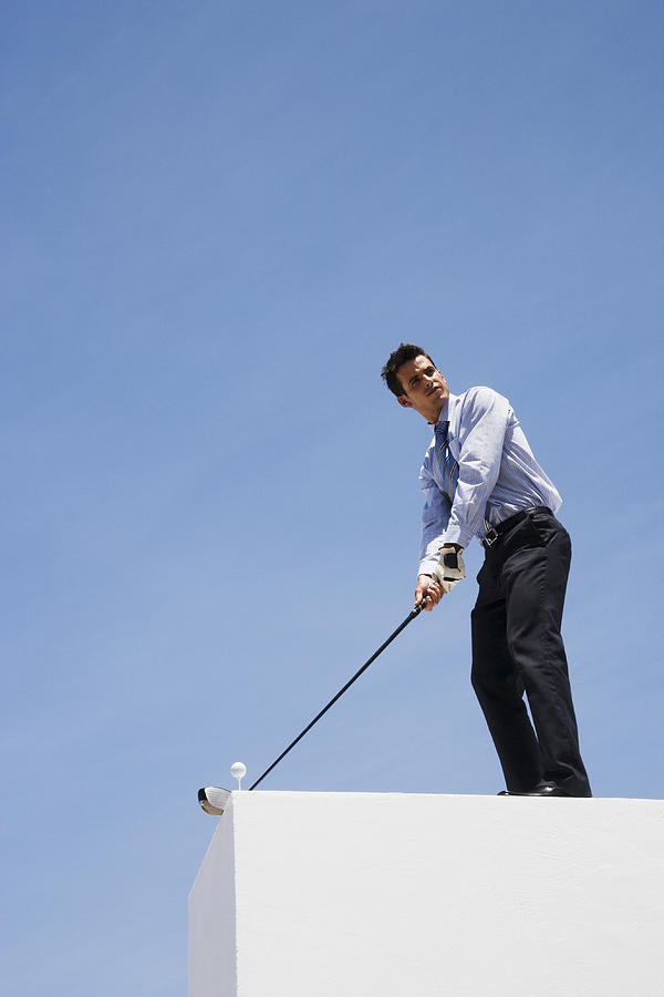 Businessman golfing on roof Photograph by Martin Barraud