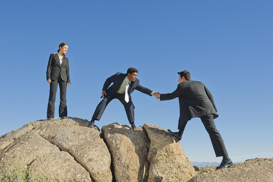 Businessman helping co-worker onto rock Photograph by Jacobs Stock Photography Ltd