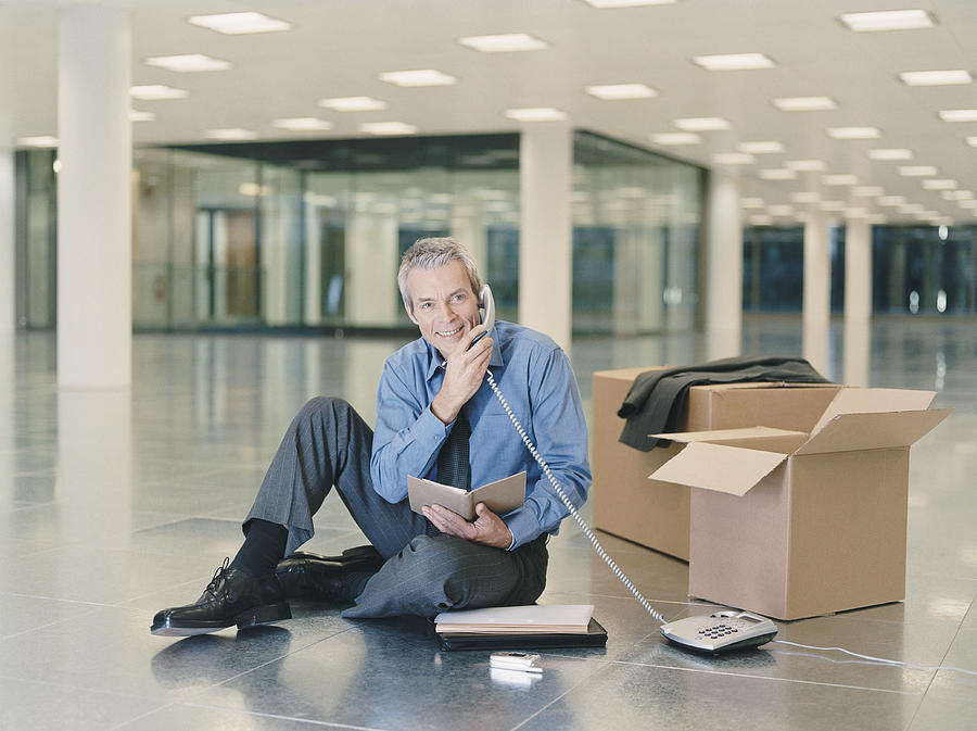 Businessman Holding a Phone Receiver Sitting in an Empty Office Photograph by Digital Vision.