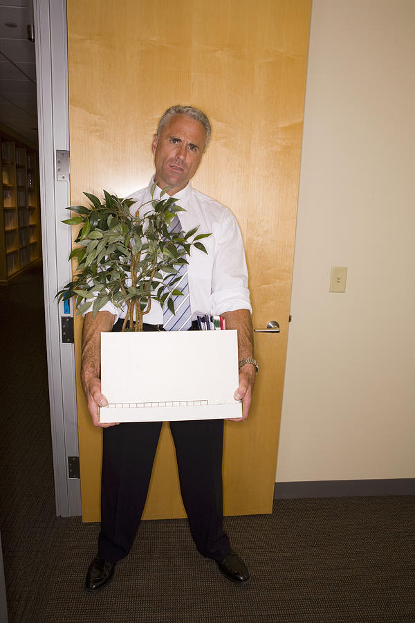 Businessman holding box and pot plant in doorway, portrait Photograph by John Giustina