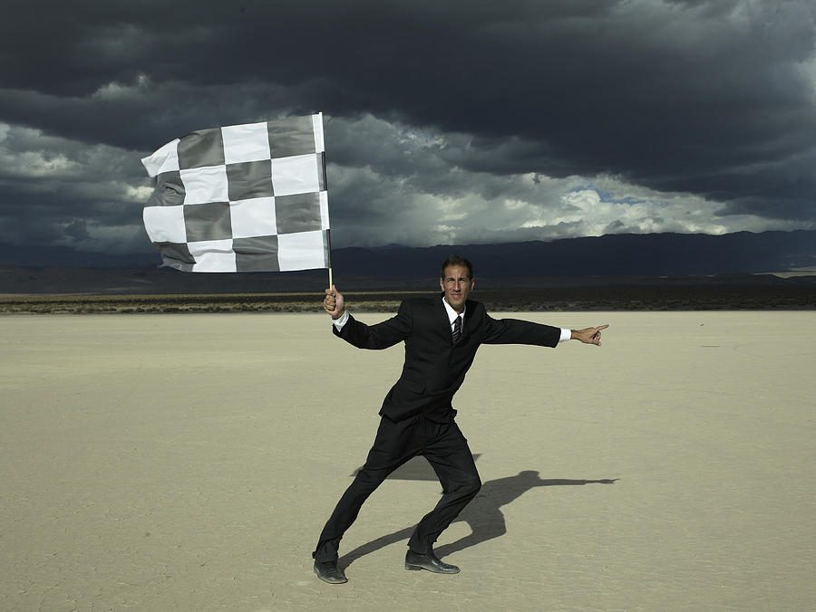 Businessman holding checkered flag in desert Photograph by Hans Neleman