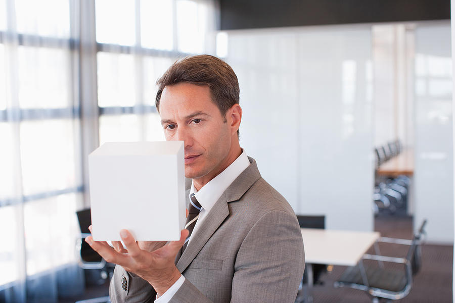 Businessman holding cube in office Photograph by Martin Barraud