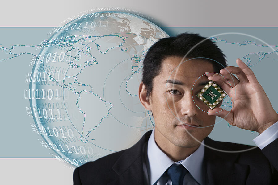 Businessman holding microchip with globe and binary code behind him Photograph by Comstock