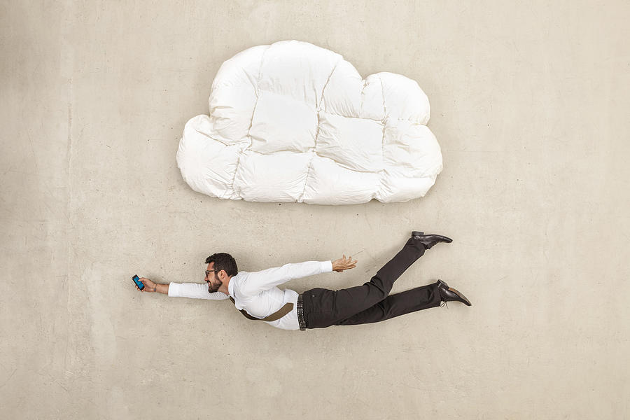 Businessman holding mobile phone and flying below cloud shape pillow Photograph by Westend61