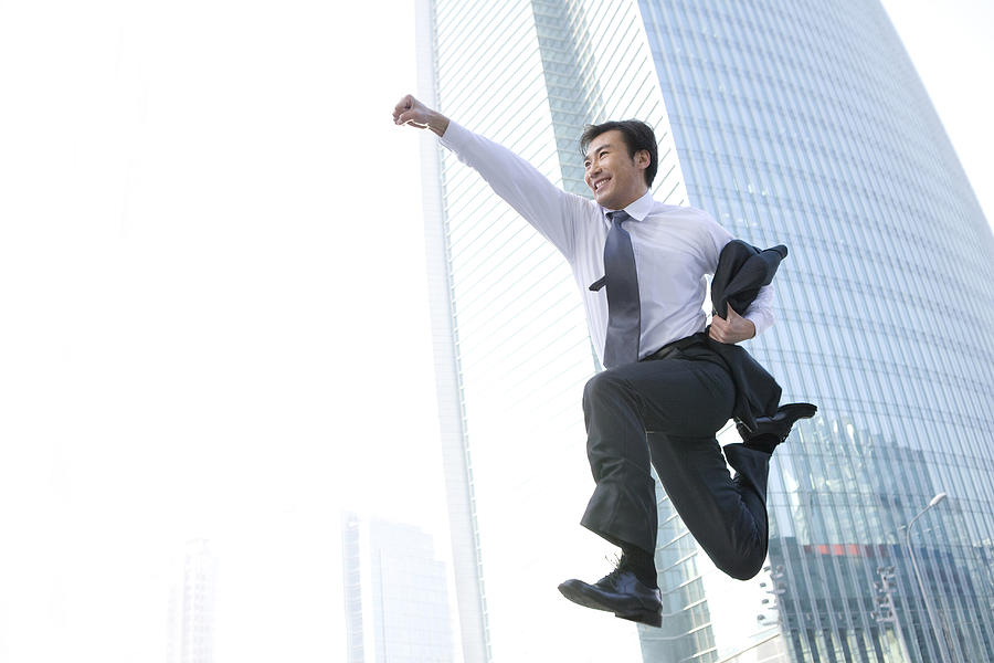 Businessman jumping in front of tall building Photograph by Lane Oatey