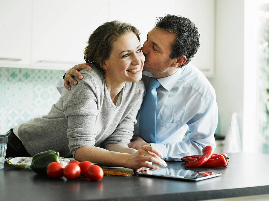 Businessman kissing wife in kitchen Photograph by Soren Hald