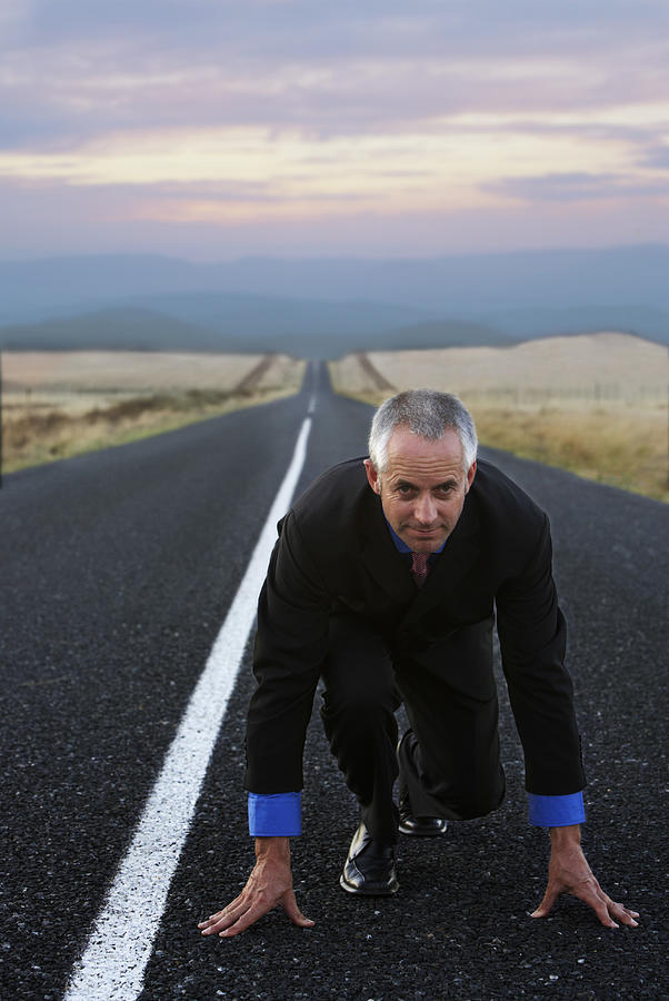 Businessman Kneeling on a Remote Road in Preparation for a Race Photograph by John Cumming