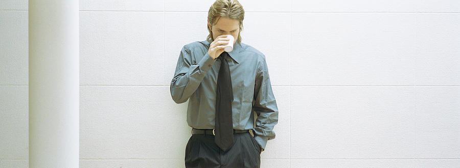 Businessman leaning against wall, drinking coffee, panoramic Photograph by Matthieu Spohn