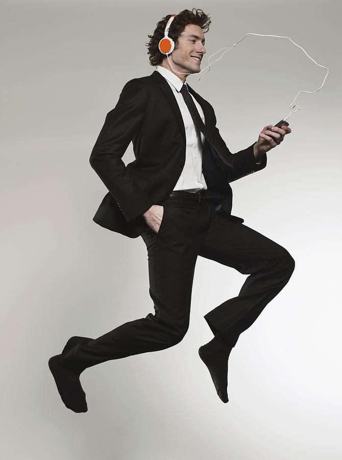 Businessman listening music and jumping, smiling Photograph by Westend61