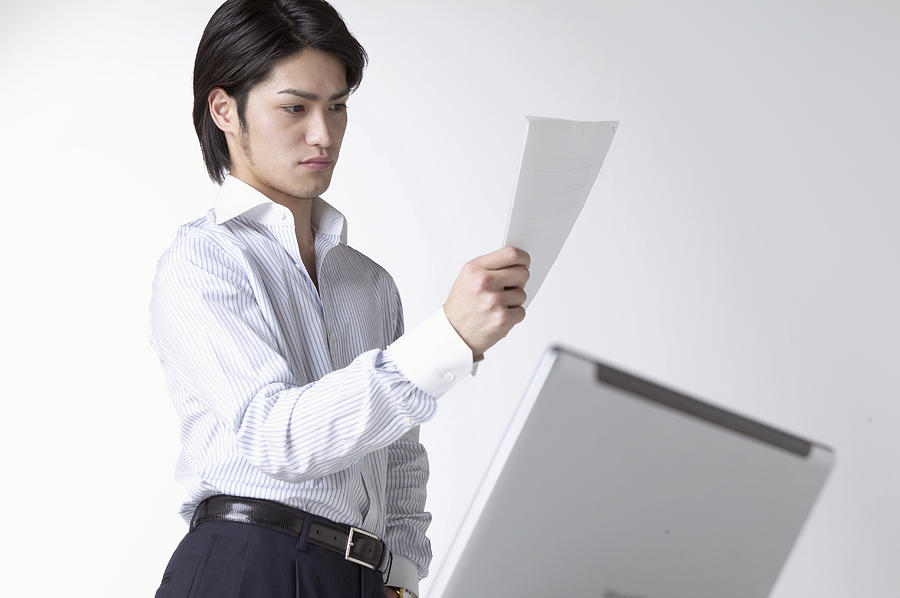 Businessman Looking at a Document With a Laptop in the Foreground Photograph by Mash