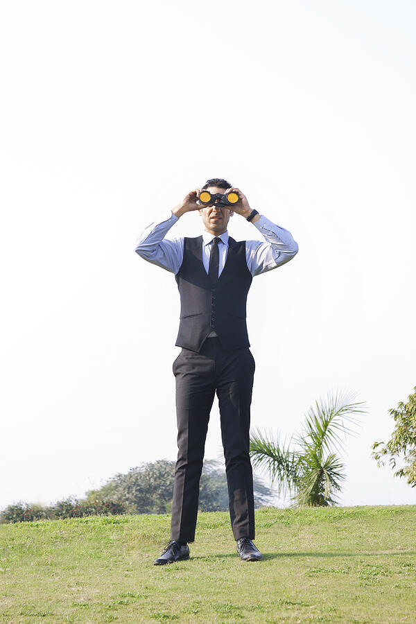 Businessman looking through binoculars , INDIA , DELHI Photograph by IndiaPix/IndiaPicture