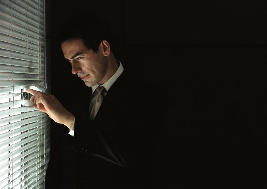 Businessman looking through venetian blinds, portrait Photograph by Laurence Mouton