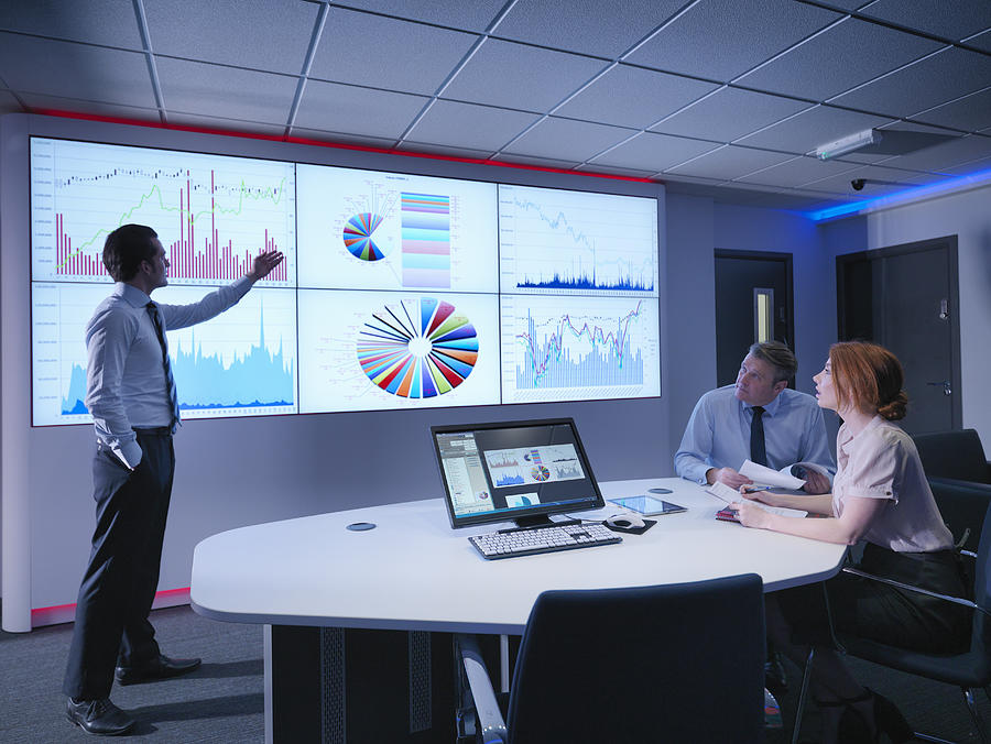 Businessman making presentation to colleagues in front of graphs on screen Photograph by Monty Rakusen