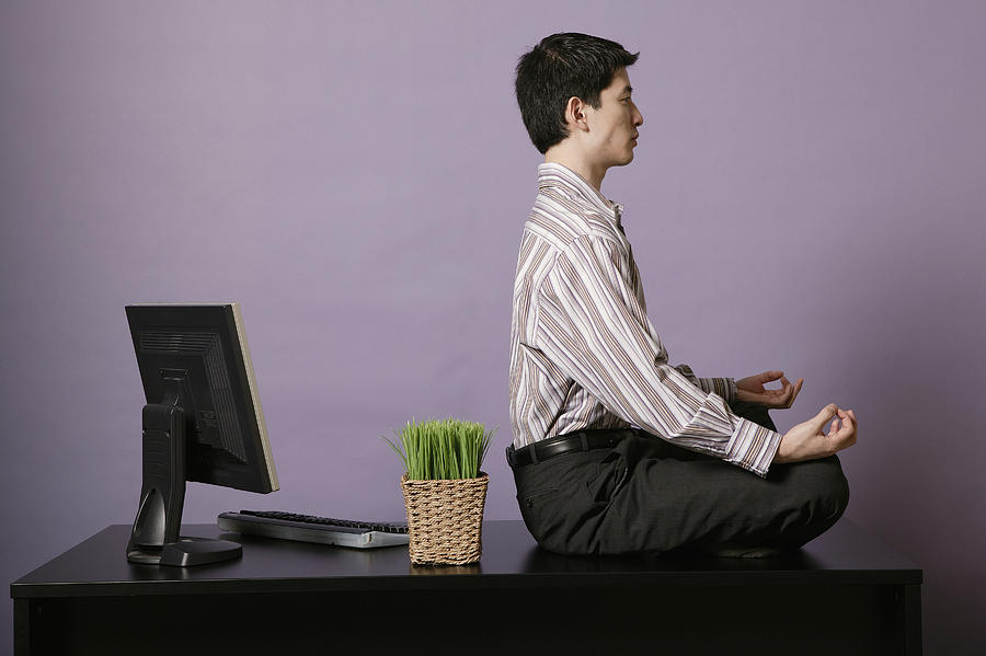 Businessman meditating on top of desk Photograph by Comstock Images