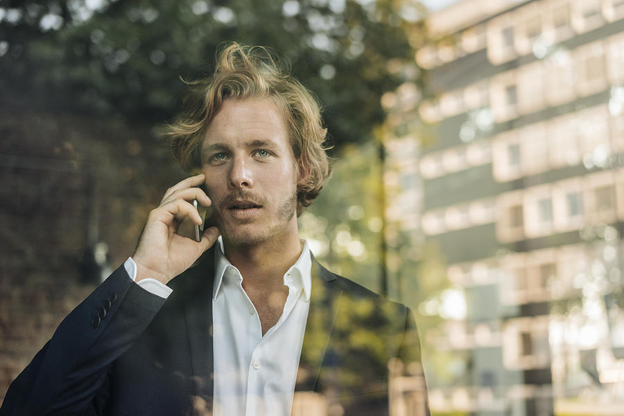 Businessman on cell phone behind windowpane Photograph by Westend61