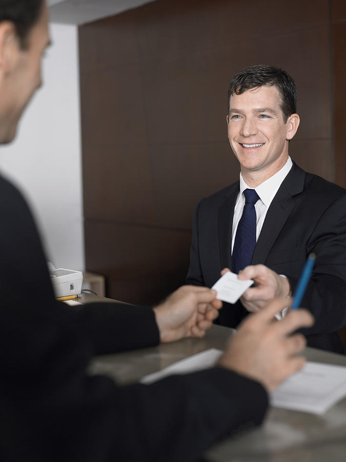 Businessman Passes a Business Card at a Reception Desk Photograph by Digital Vision.