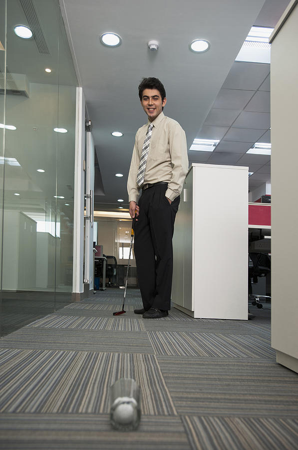Businessman playing golf in office Photograph by Uniquely India