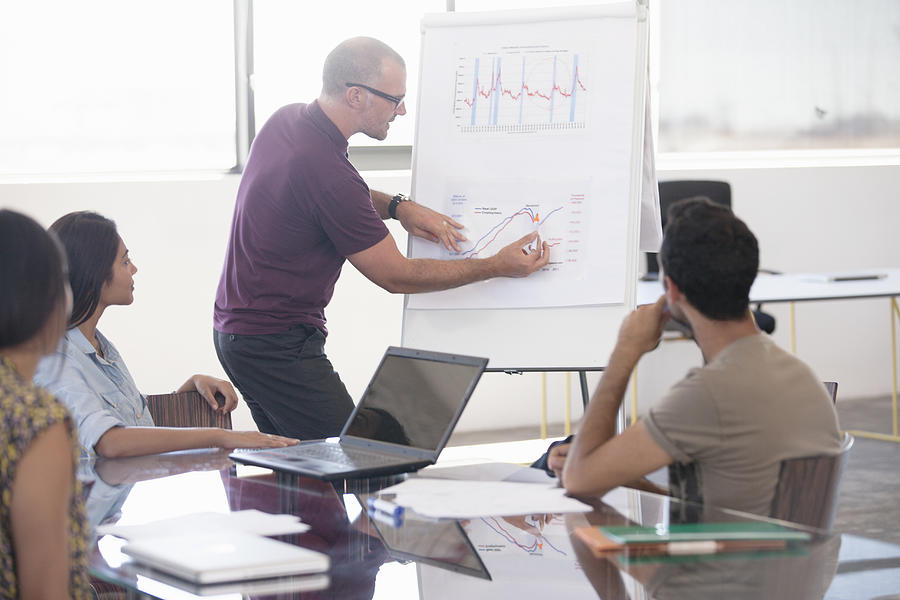 Businessman pointing at flip chart in meeting Photograph by David Lees