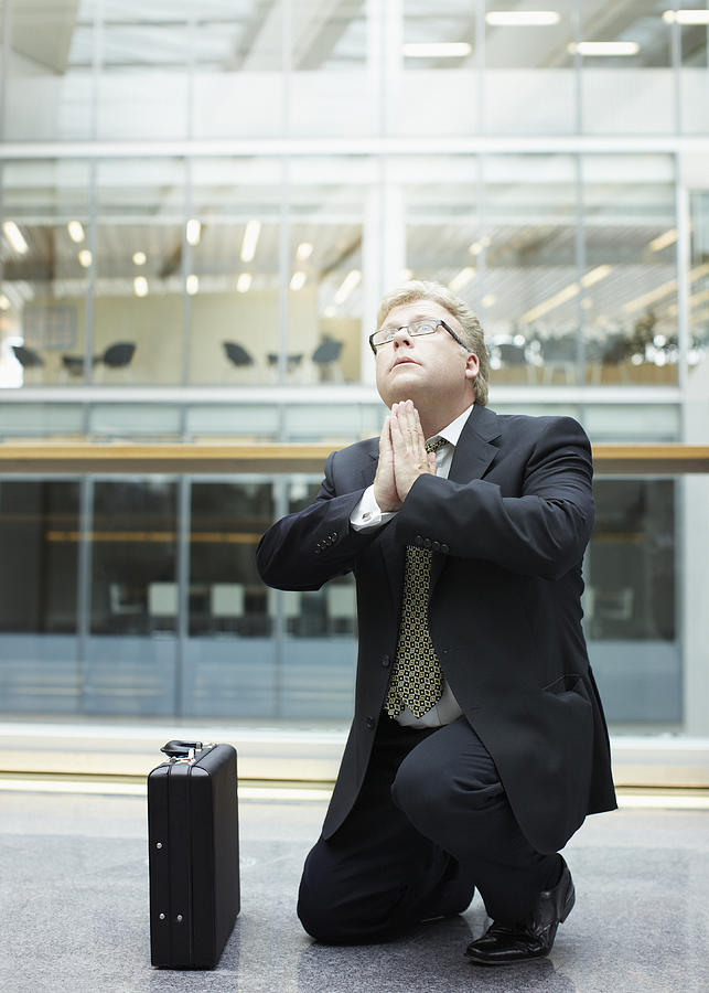 Businessman praying in building lobby Photograph by Paul Bradbury