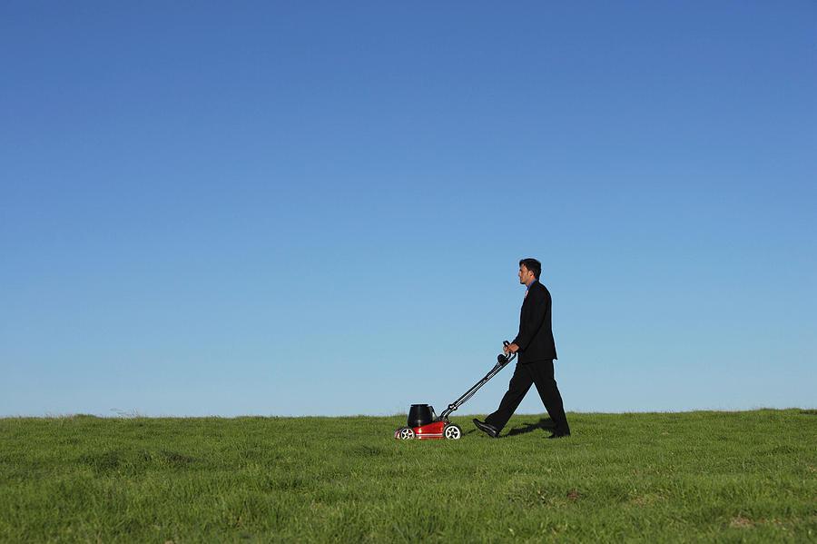 Businessman Pushing a Lawnmower Over Grass Photograph by Digital Vision.