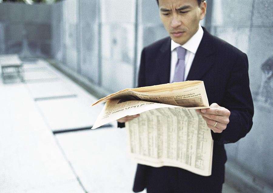 Businessman reading newspaper, waist up, long shot Photograph by Eric Audras