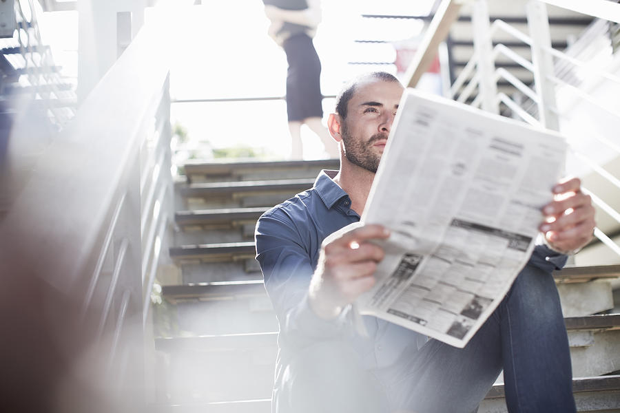 Businessman reading newspapers on staircase Photograph by Zero Creatives