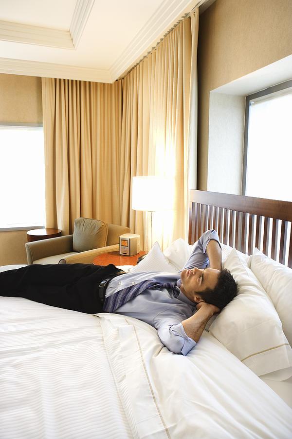 Businessman relaxing on bed in hotel room Photograph by Jupiterimages