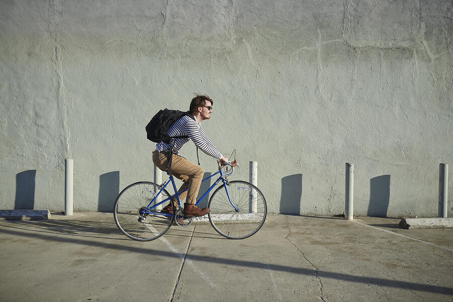 Businessman riding bicycle along concrete wall Photograph by The Good Brigade