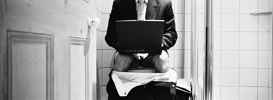 Businessman seated on the toilet, with a laptop computer, B&W Photograph by Teo Lannie
