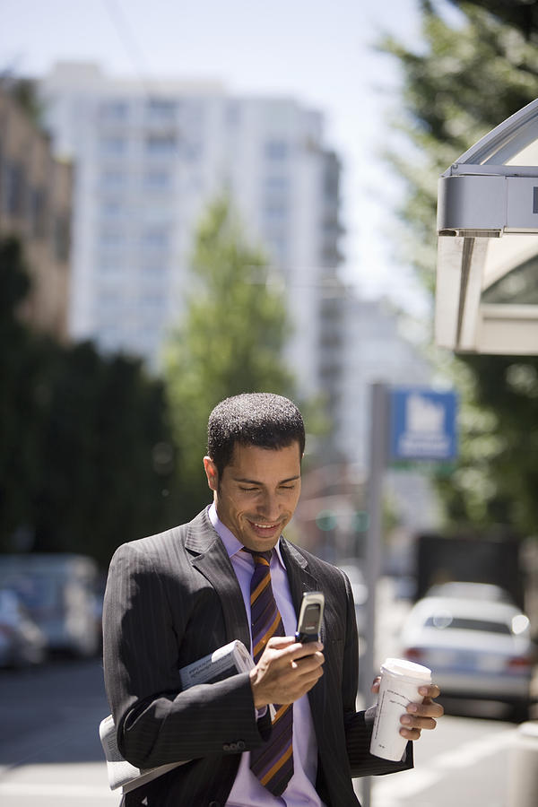 Businessman sending text messages on city street Photograph by John Giustina