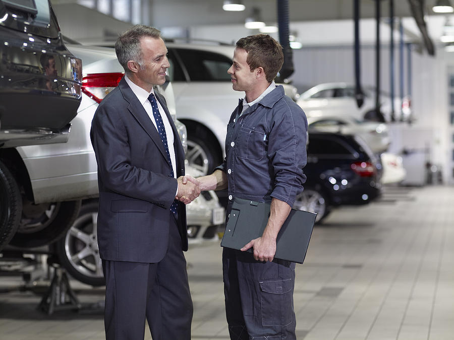 Businessman shaking hands with mechanic in auto repair shop Photograph by Adam Gault