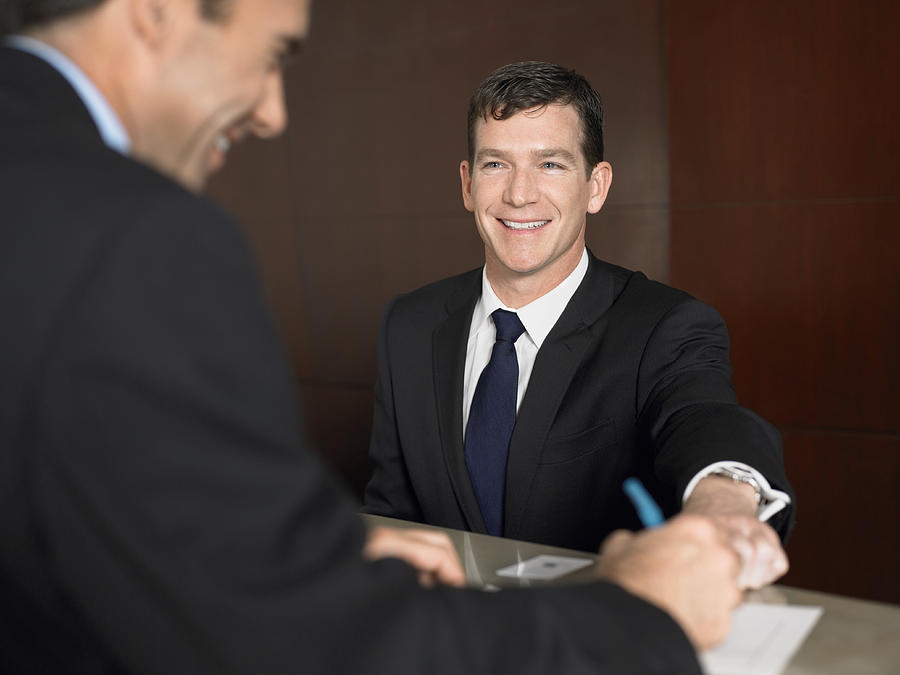 Businessman Signing a Document at a Reception Desk Photograph by Digital Vision.