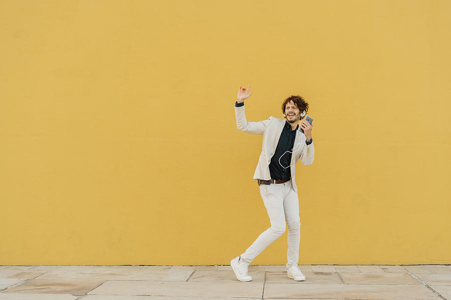 Businessman singing and dancing in front of yellow wall listening music with headphones and smartphone Photograph by Westend61 Businessman singing and dancing in front of yellow wall listening music with headphones and smartphone Photograph by Westend61