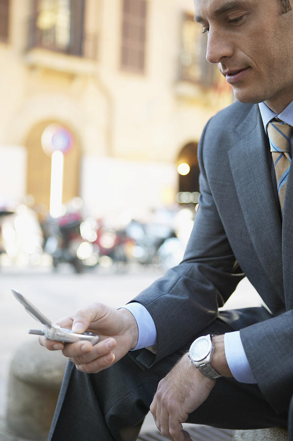 Businessman Sits in an Urban Setting Texting on His Mobile Phone Photograph by Digital Vision.