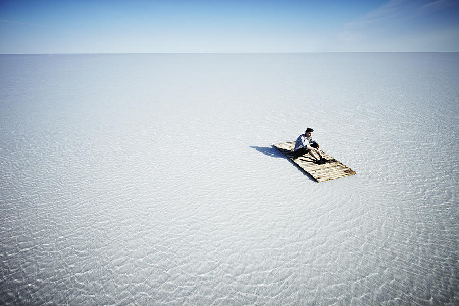 Businessman sitting alone on life raft Photograph by Thomas Barwick
