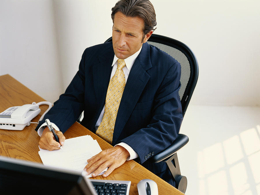 Businessman sitting at desk and writing, elevated view Photograph by Stockbyte