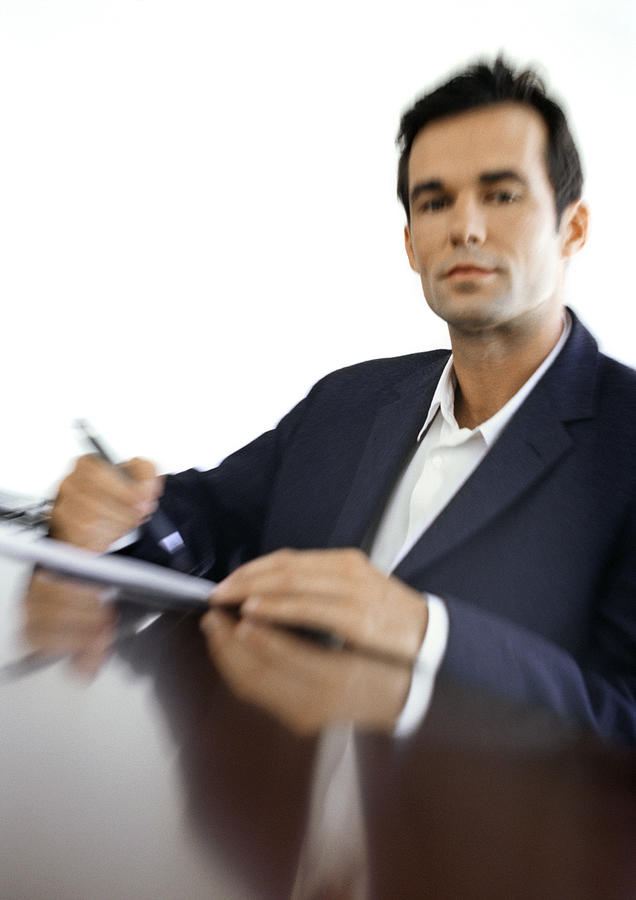Businessman sitting at desk, blurred, portrait Photograph by Vincent Hazat