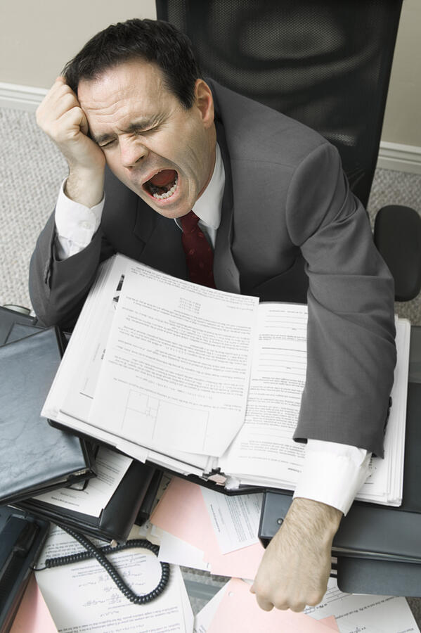 Businessman sitting behind a desk yawning Photograph by Photodisc