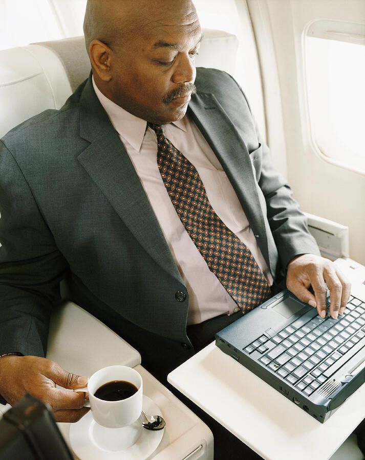 Businessman Sitting in a Seat in an Aircraft Using his Laptop Photograph by Digital Vision.