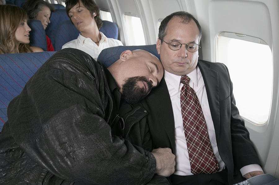 Businessman Sitting in an Aeroplane Trapped by a Man Sleeping by His Side Photograph by Digital Vision.