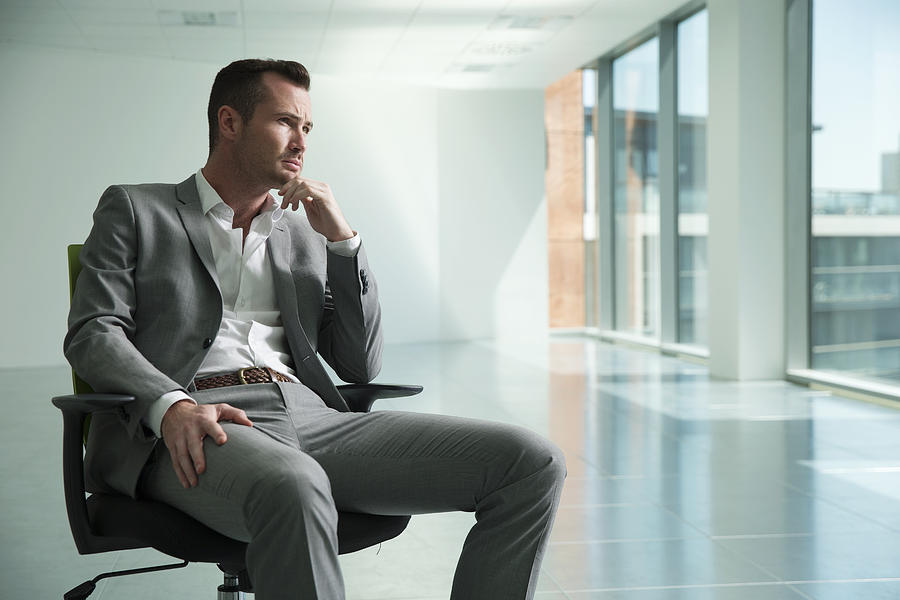 Businessman sitting in chair in empty office space, thoughtful expression Photograph by Igor Emmerich