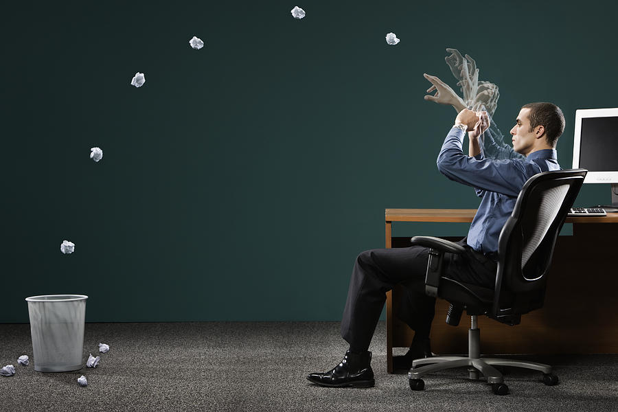 Businessman sitting in office, throwing paper ball in dustbin Photograph by Siri Stafford