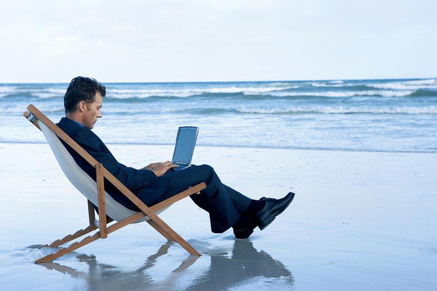 Businessman Sitting on a Beach in a Deck Chair Working on His Laptop Photograph by John Cumming