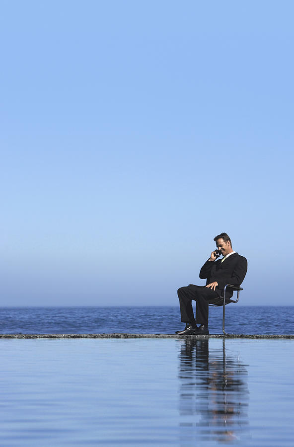Businessman Sitting on a Chair by the Sea and Using a Mobile Phone Photograph by John Cumming