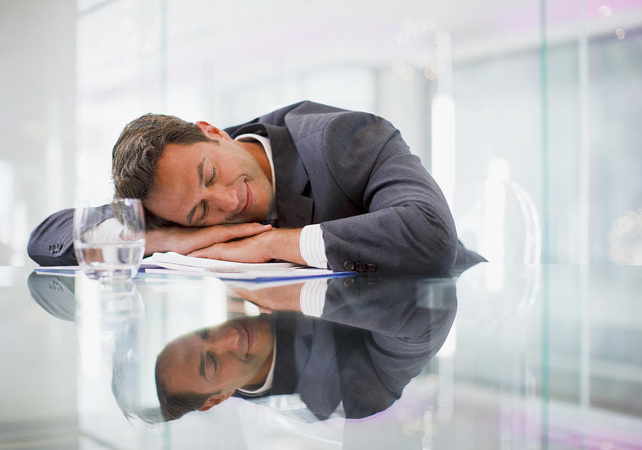 Businessman sleeping at desk in office Photograph by Paul Bradbury
