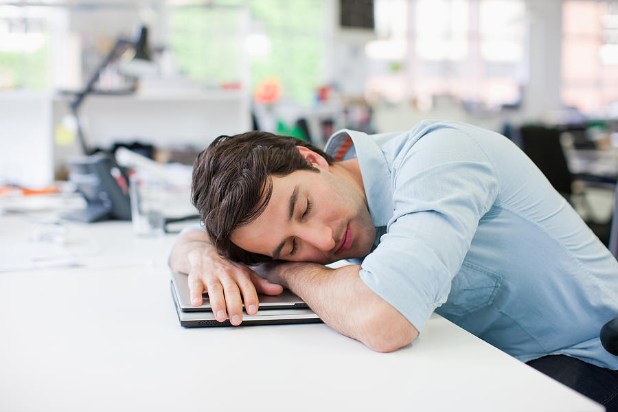 Businessman sleeping on laptop at desk in office Photograph by Paul Bradbury