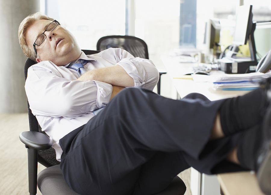 Businessman sleeping with feet up at desk Photograph by Paul Bradbury