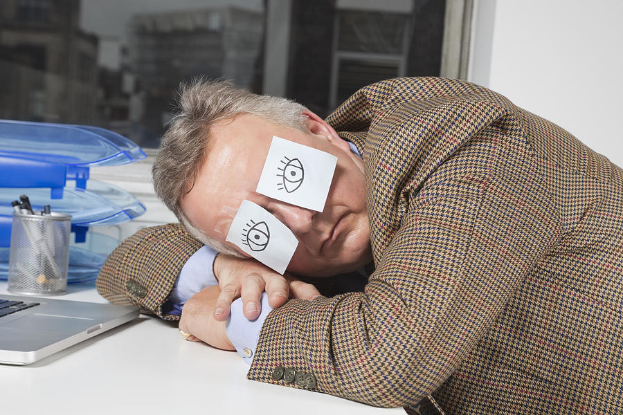 Businessman sleeping with sticky notes on eyes at desk in office Photograph by Moodboard
