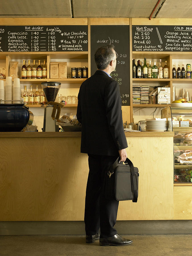 Businessman standing at counter in cafe, rear view Photograph by Mel Yates